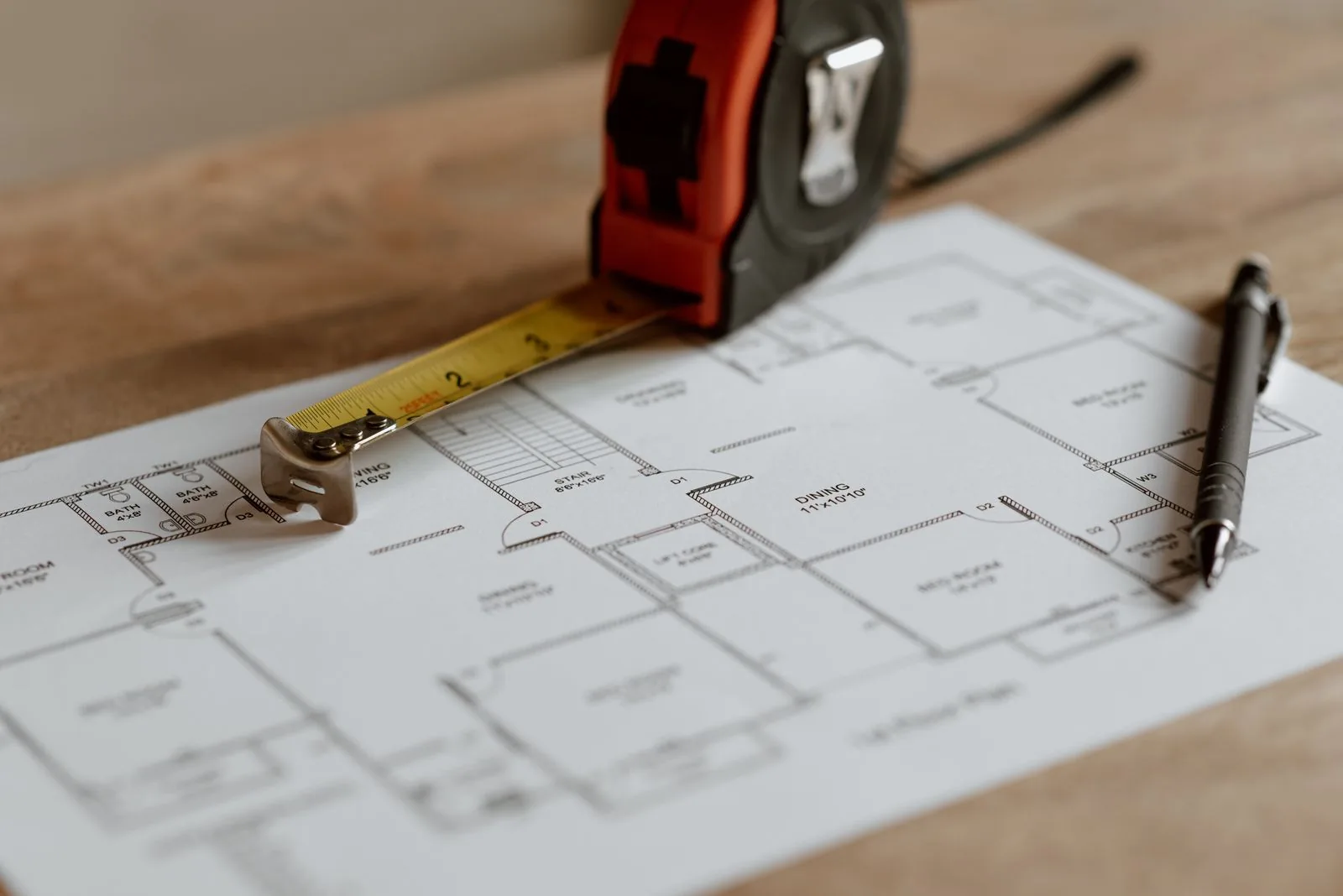 Measuring tape, floor plan and pencil arranged on a wooden work surface
