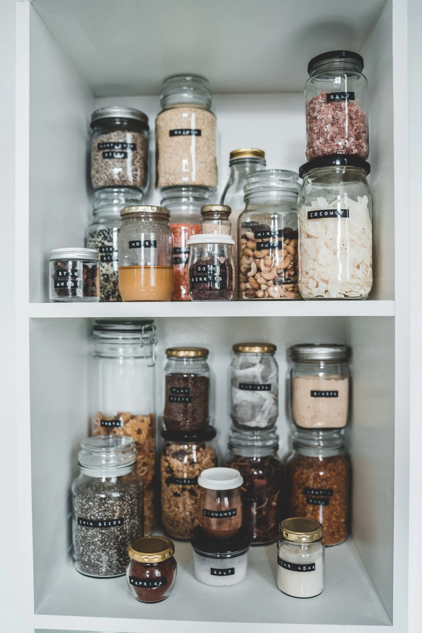 Glass food jars arranged neatly on white pantry shelves